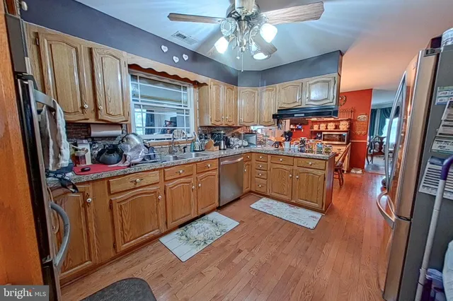 a kitchen with stainless steel appliances a sink dishwasher a refrigerator a microwave oven with wooden floor and cabinets