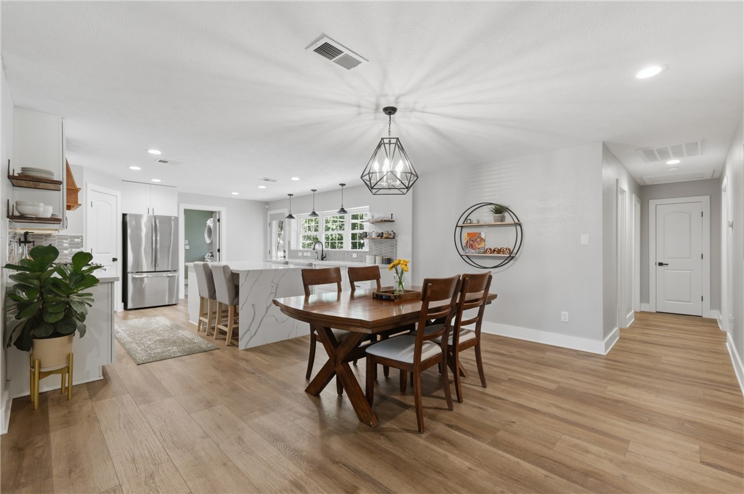 515 Crescent Drive Bryan, TX 77801 - Photo 11 of 43 Open-concept kitchen and dining area featuring wood-finish flooring, white cabinetry, a waterfall-edge island with seating, and a geometric pendant light fixture