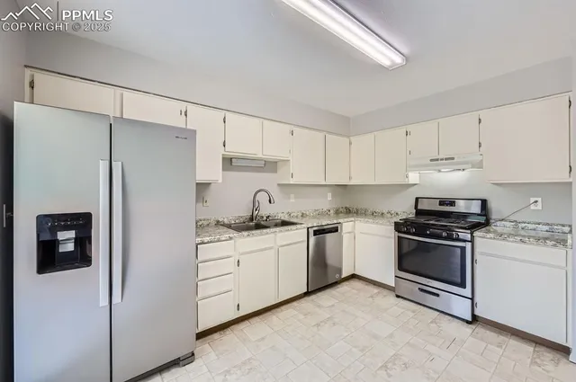 a kitchen with stainless steel appliances granite countertop a refrigerator a stove a sink and white cabinets