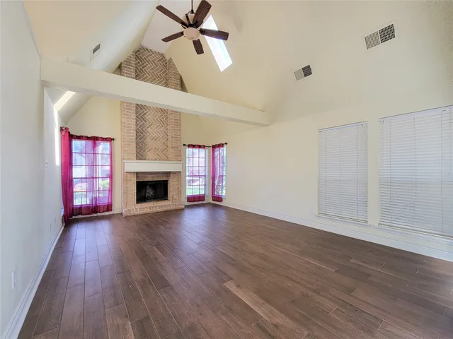 an empty room with wooden floor fireplace and windows