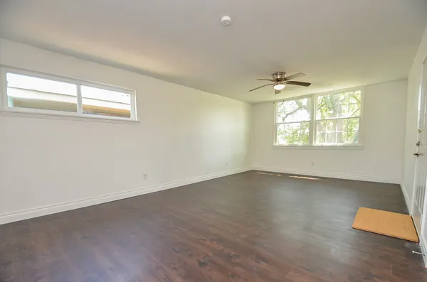 an empty room with wooden floor chandelier fan and windows