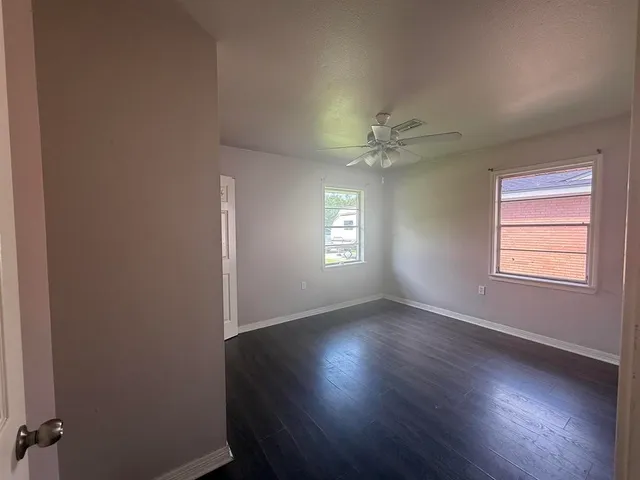 an empty room with wooden floor fan and windows