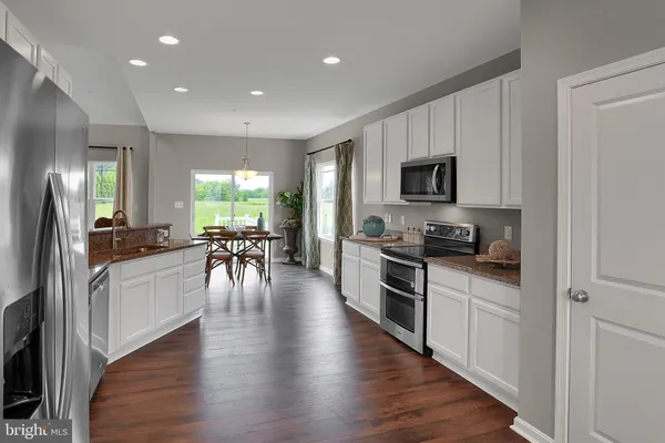 a kitchen with stainless steel appliances kitchen island granite countertop a stove top oven a sink a dining table and chairs with wooden floor