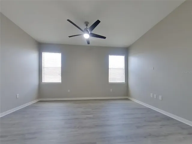 an empty room with wooden floor fan and windows