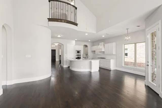 a view of an empty room and kitchen with wooden floor