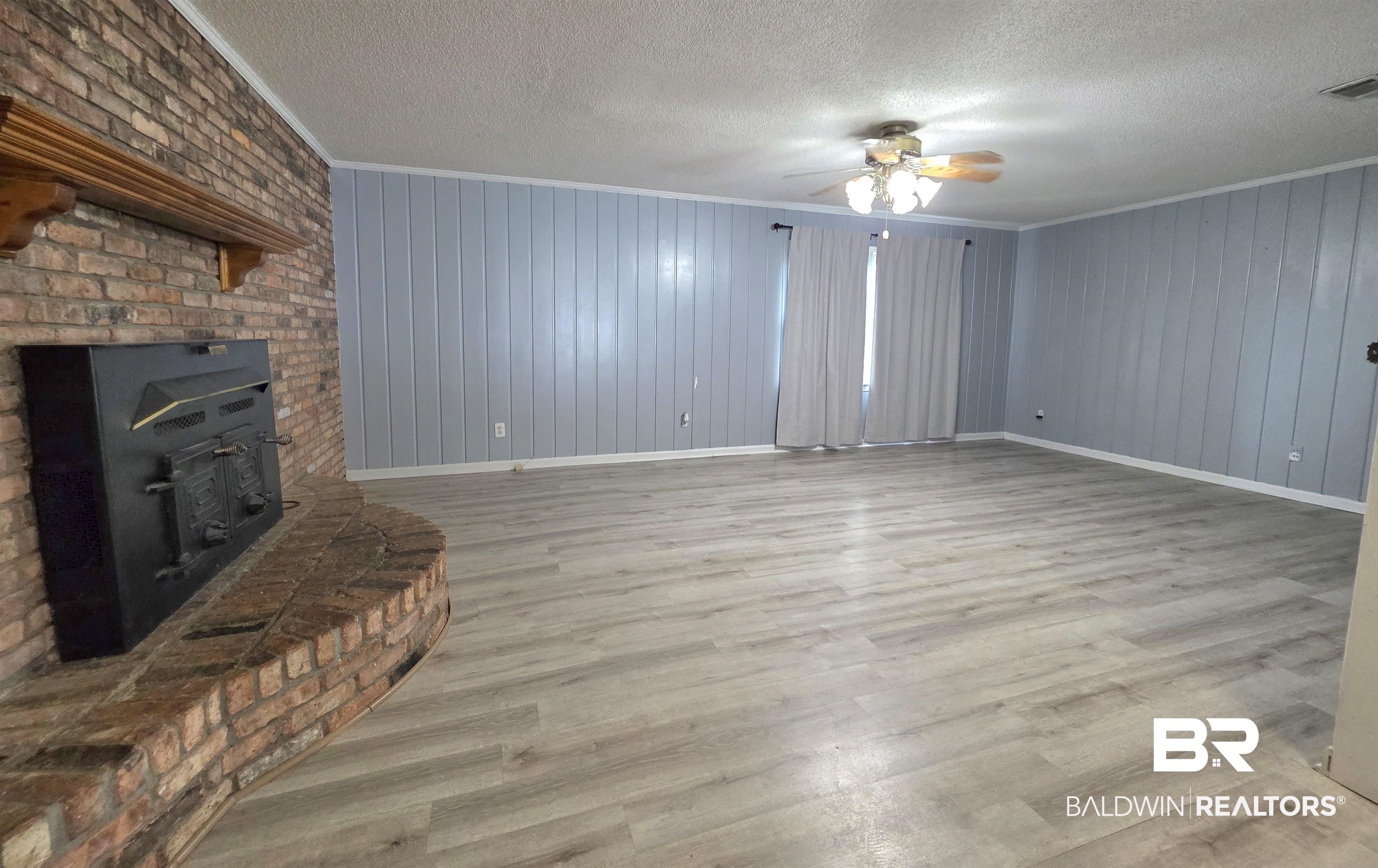 558 Stanton Road Atmore, AL 36502 - Photo 5 of 29 Spacious room featuring a brick fireplace with a wood mantle, wood-finish flooring, light blue panel walls, and a ceiling fan