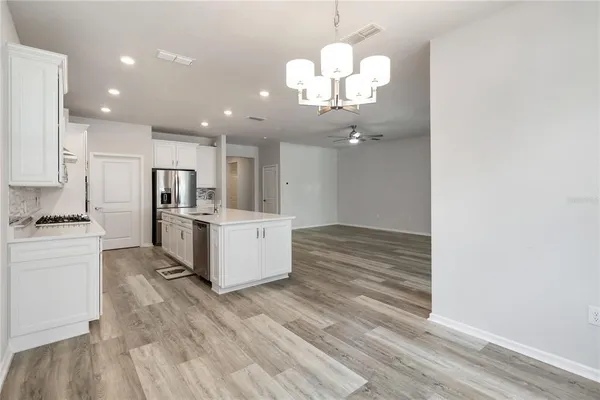 a large kitchen with kitchen island a stove a sink dishwasher a refrigerator and white cabinets with wooden floor