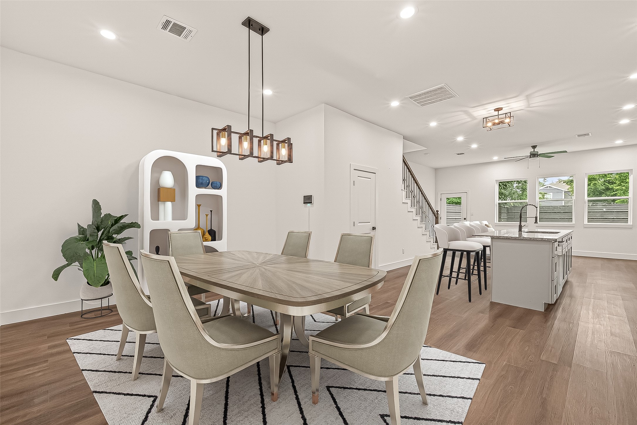6808 Madrid Street Houston, TX 77021 - Photo 2 of 31 This photo showcases a modern, open-concept dining and kitchen area with elegant lighting fixtures, sleek engineer wood flooring, and large windows allowing natural light. The kitchen features an island with bar seating, and the dining area is stylishly furnished, providing a warm and inviting atmosphere.- Virtual Staging