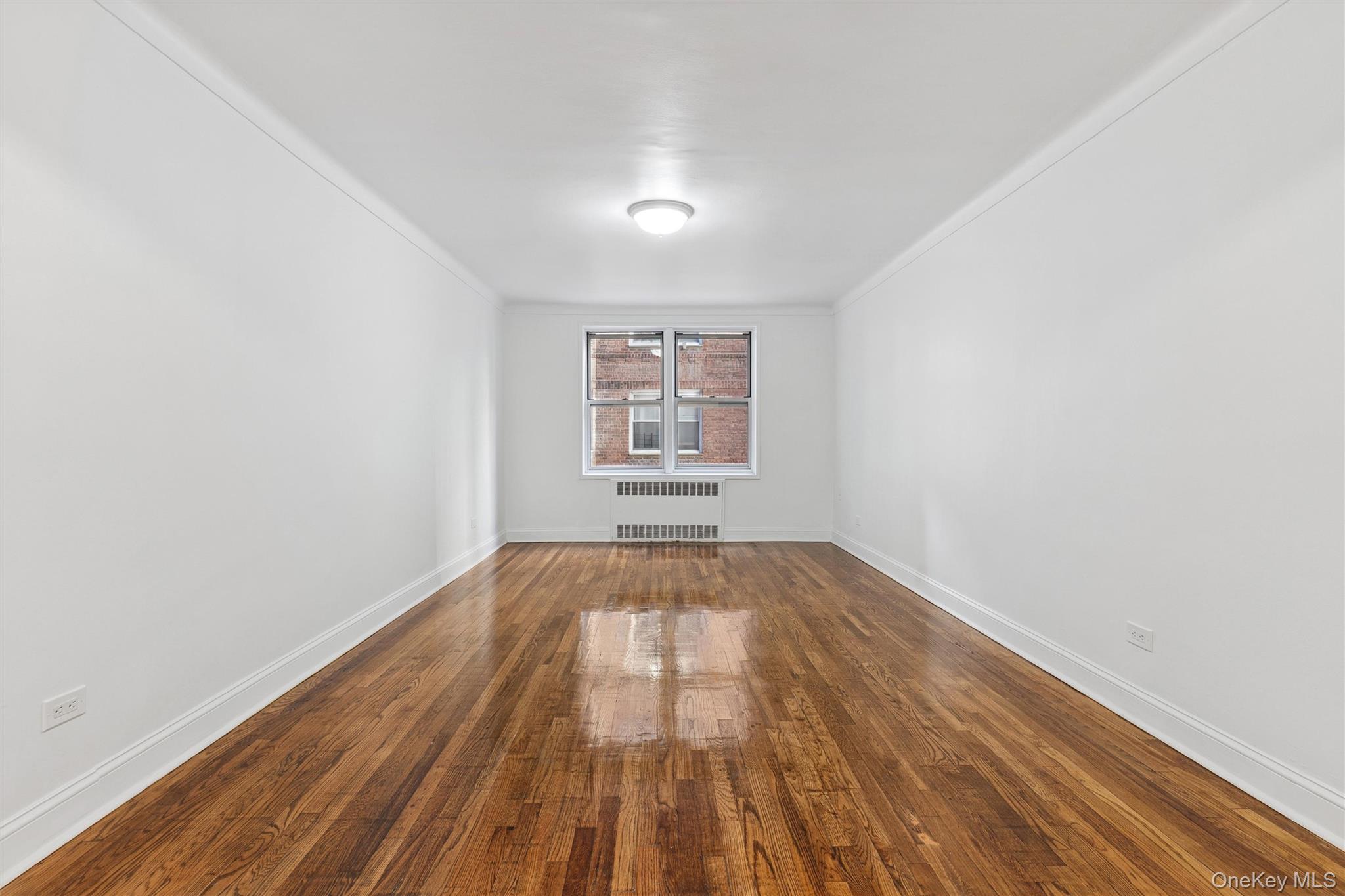 67-12 Yellowstone Boulevard, Unit B16 Queens, NY 11375 - Photo 4 of 15 Empty room featuring dark wood-type flooring, crown molding, and radiator heating unit