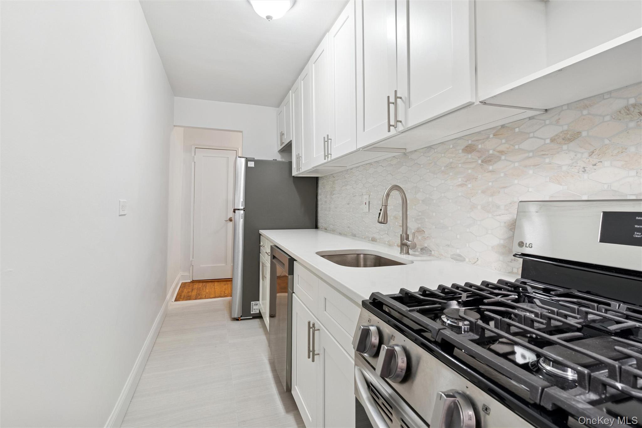 67-12 Yellowstone Boulevard, Unit B16 Queens, NY 11375 - Photo 9 of 15 Kitchen featuring appliances with stainless steel finishes, decorative backsplash, white cabinets, and light stone counters