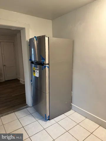 a view of a refrigerator in kitchen and an empty room in wooden floor