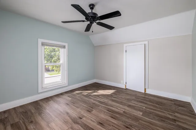 an empty room with wooden floor fan and windows