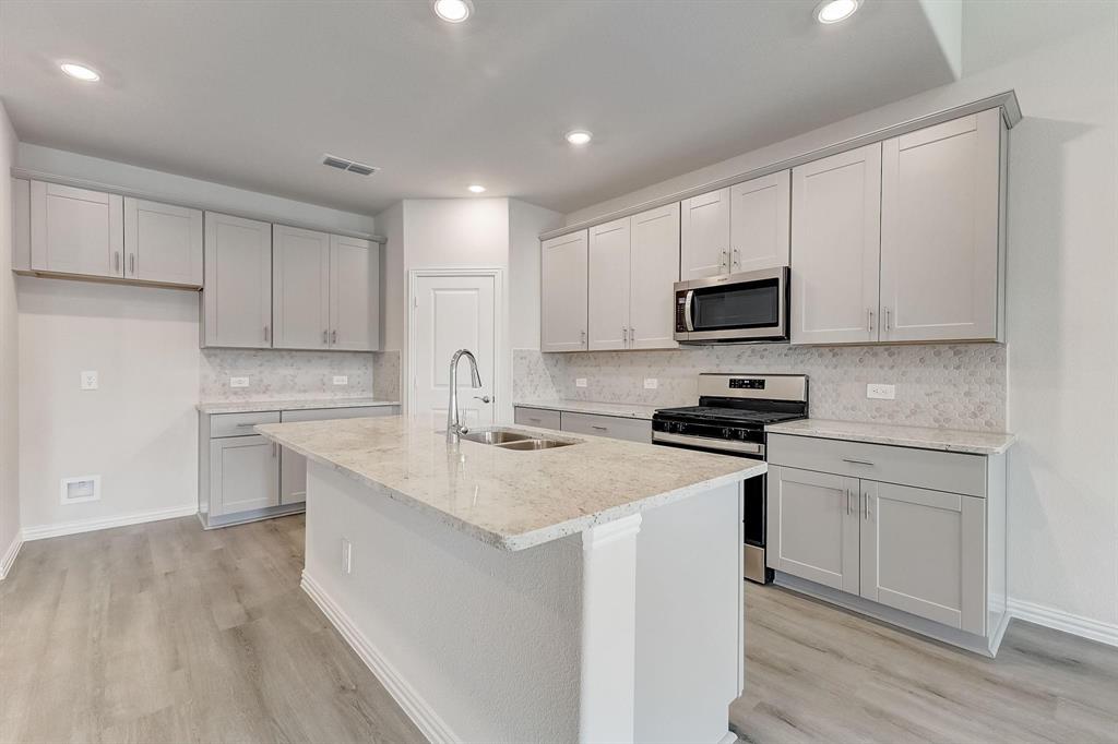 1405 Winters Way McKinney, TX 75071 - Photo 1 of 32 Kitchen with sink, appliances with stainless steel finishes, light stone counters, a center island with sink, and light wood-type flooring