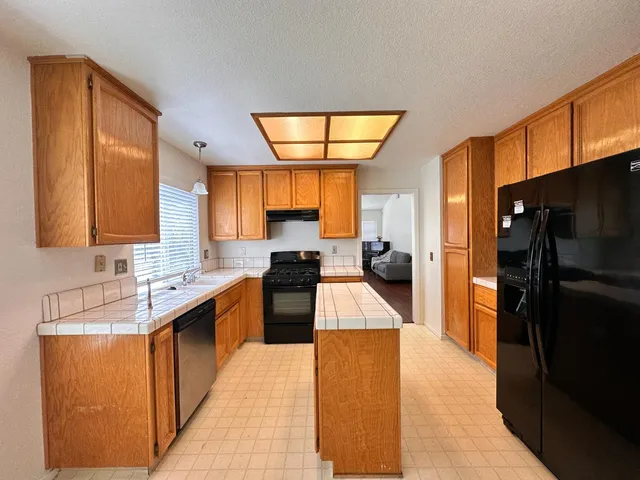 a large kitchen with stainless steel appliances kitchen island granite countertop a refrigerator a sink dishwasher a stove and a dining table with wooden floor