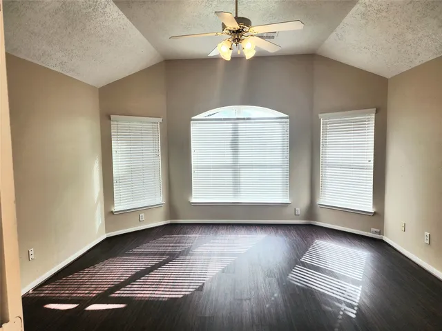 an empty room with wooden floor chandelier fan and windows