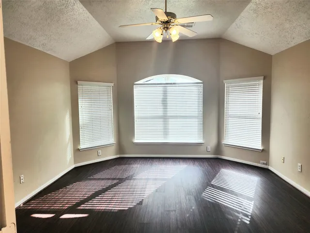 an empty room with wooden floor chandelier fan and windows