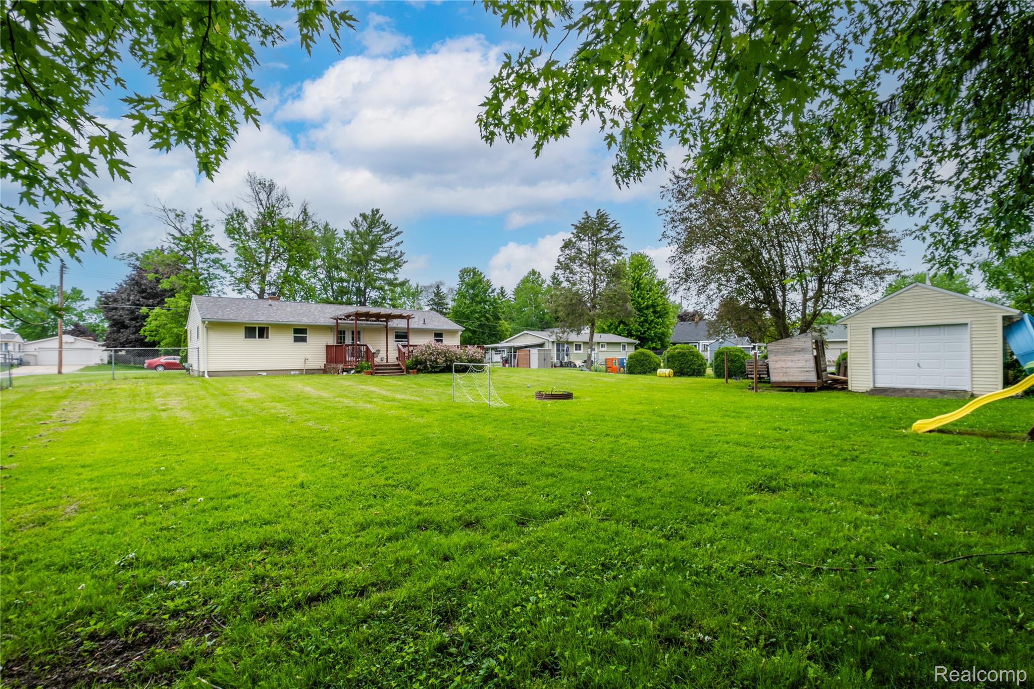 7800 Maple Street Birch Run, MI 48415 - Photo 25 of 29 Expansive green lawn with a detached garage and a light-toned ranch-style home featuring a rear deck