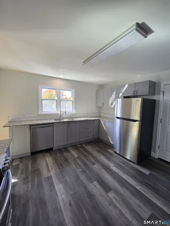a view of an empty room with wooden floor and a kitchen