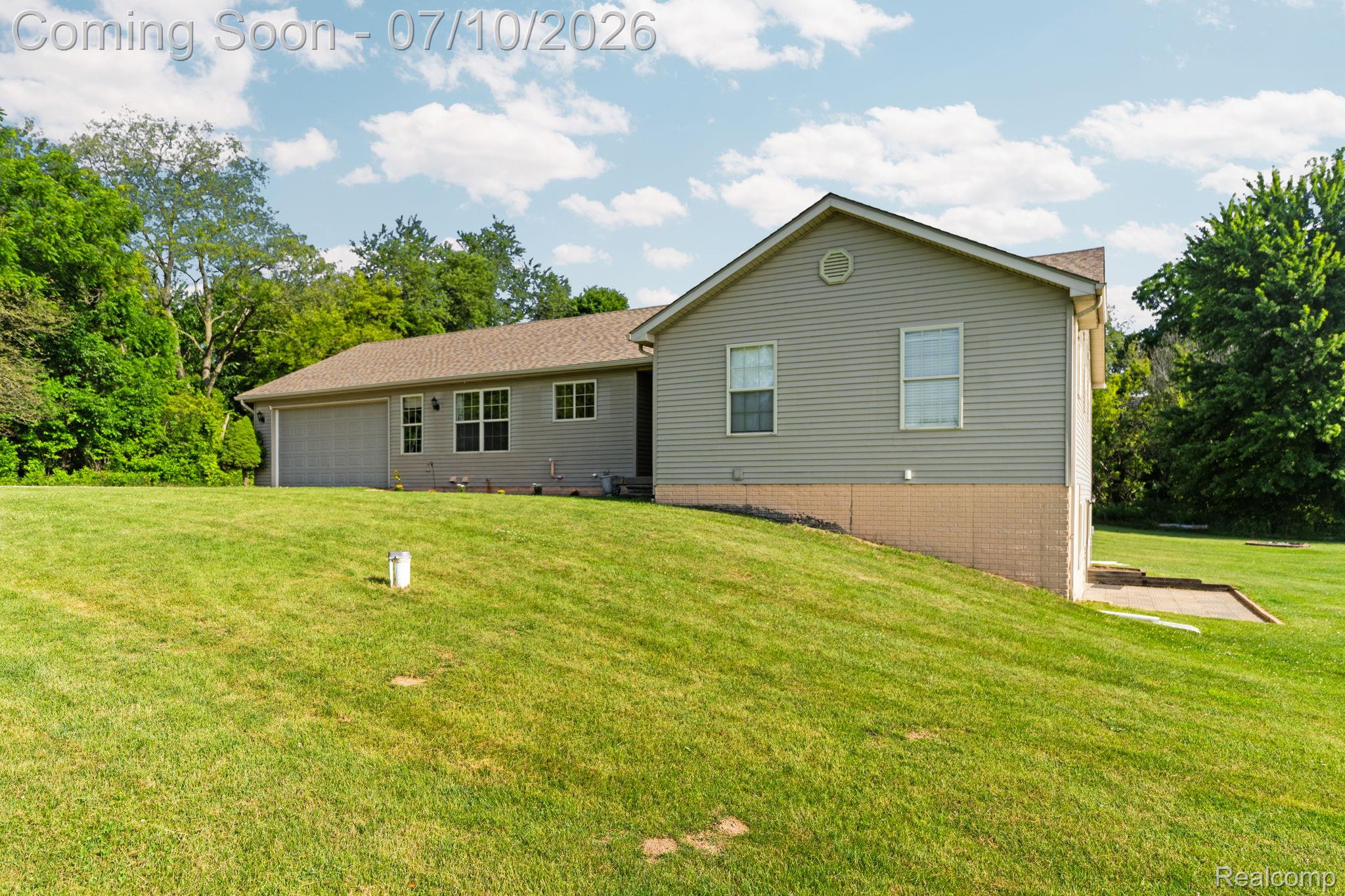 3144 North Nicholson Road Fowlerville, MI 48836 - Photo 21 of 70 Expansive green lawn bordering the property, featuring a gray siding exterior, an attached garage, and a walk-out lower level patio