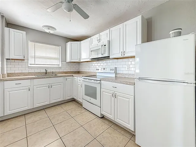 a kitchen with white cabinets a sink appliances and a window