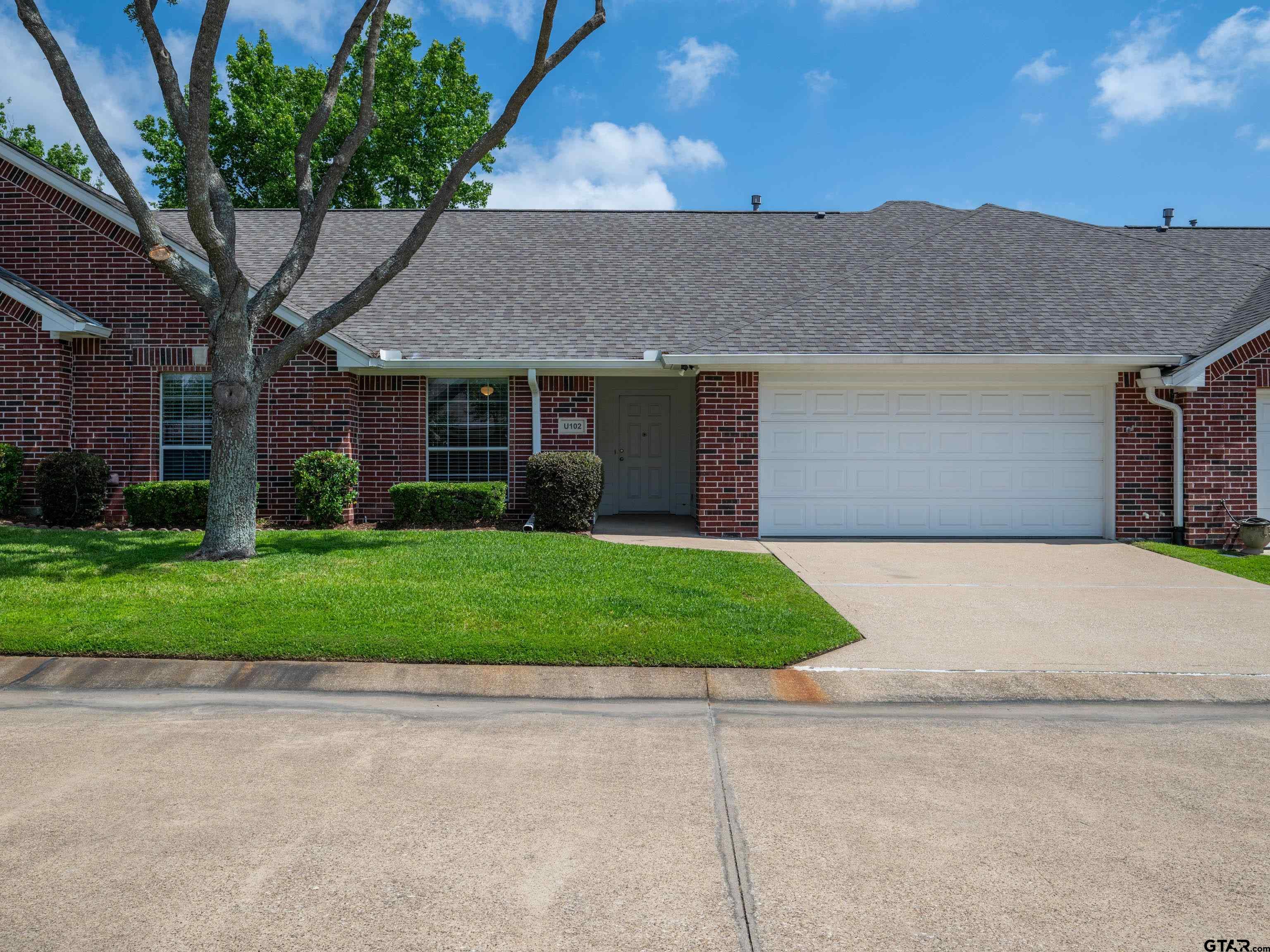 a brick house with a yard plants and big trees