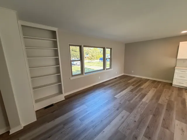 an empty room with wooden floor closet and windows