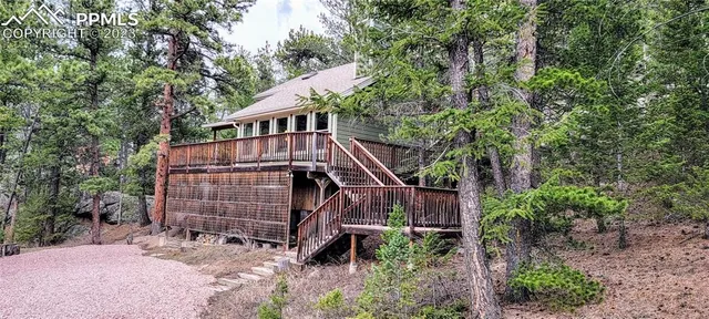 a view of a wooden house with a small yard and large trees