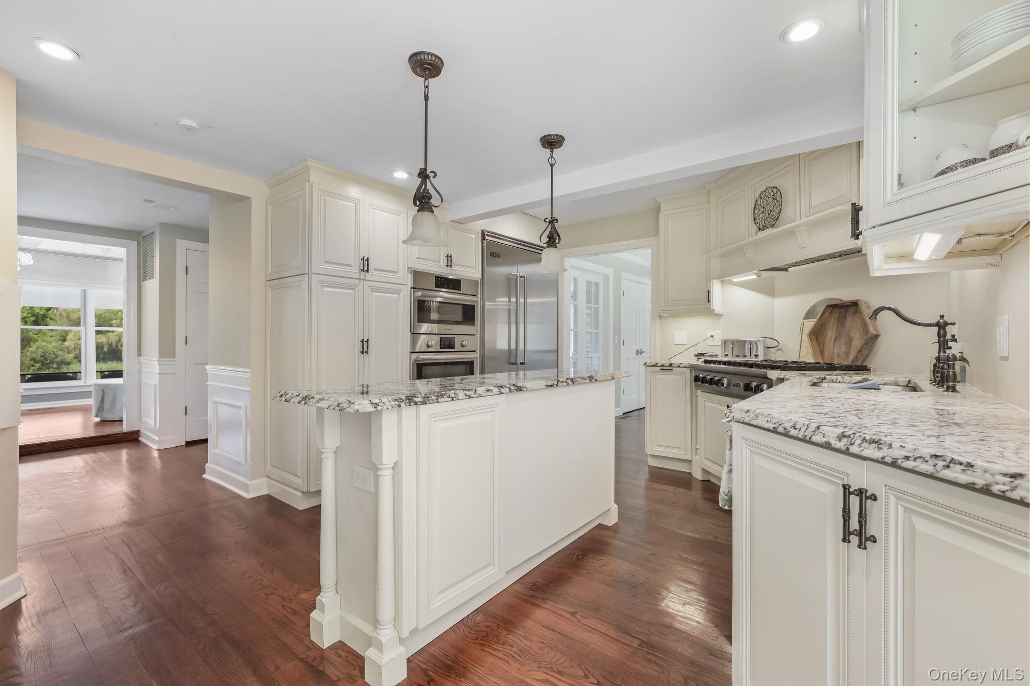 777 Armonk Road Mount Kisco, NY 10549 - Photo 8 of 44 Kitchen featuring light stone countertops, hanging light fixtures, a kitchen island, dark wood-type flooring, and a decorative wall