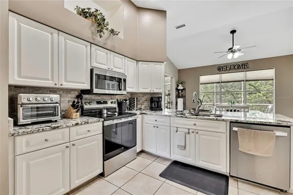 a kitchen with granite countertop white cabinets white appliances a sink and dishwasher with wooden floor