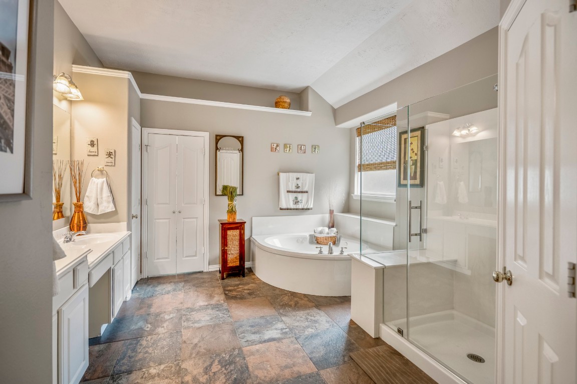 6811 PInehearth Court Spring, TX 77379 - Photo 20 of 50 The primary bath opens up with vaulted ceilings and a spacious layout, featuring a soaking tub set beneath a window, a separate glass-enclosed shower, and an extended vanity with plenty of storage. The scale here makes everyday routines feel a little more relaxed, with room to spread out and unwind.
