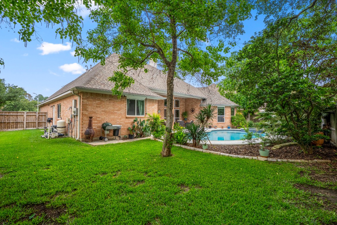 6811 PInehearth Court Spring, TX 77379 - Photo 34 of 50 Continuing across the yard, this angle shows the other side of the outdoor space—where the lawn stretches out alongside the pool and landscaping. There’s a natural balance here between open green space and the more curated poolside setting, giving the backyard a layout that feels both functional and easy to enjoy.