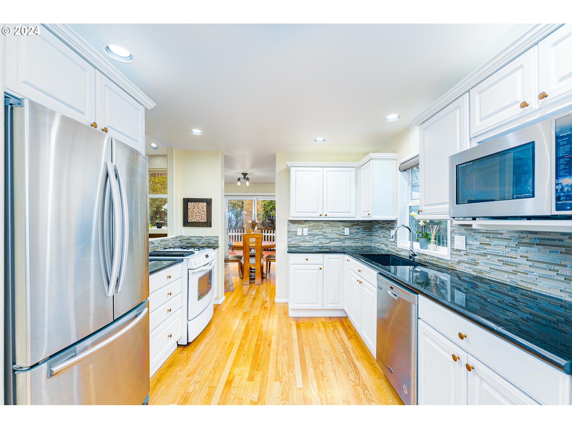 14915 Southwest Osprey Court Beaverton, OR 97007 - Photo 12 of 38 a kitchen with stainless steel appliances granite countertop a refrigerator a sink dishwasher a stove and white cabinets with wooden floor