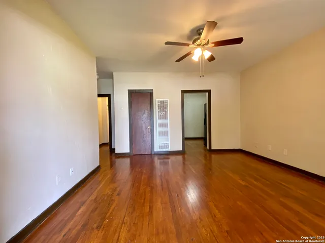 a view of an empty room with wooden floor and a ceiling fan