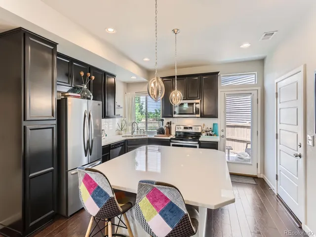 a kitchen with stainless steel appliances granite countertop a refrigerator a sink dishwasher a stove and a dining table with wooden floor