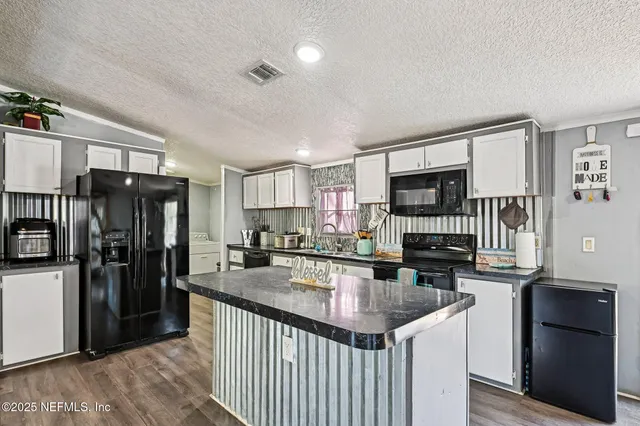 a kitchen with stainless steel appliances kitchen island granite countertop a refrigerator oven a sink dishwasher and white cabinets with wooden floor