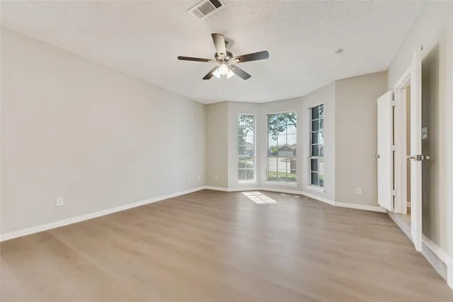 an empty room with wooden floor fan and windows