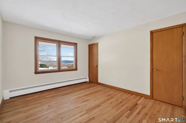 a view of an empty room with window and wooden floor