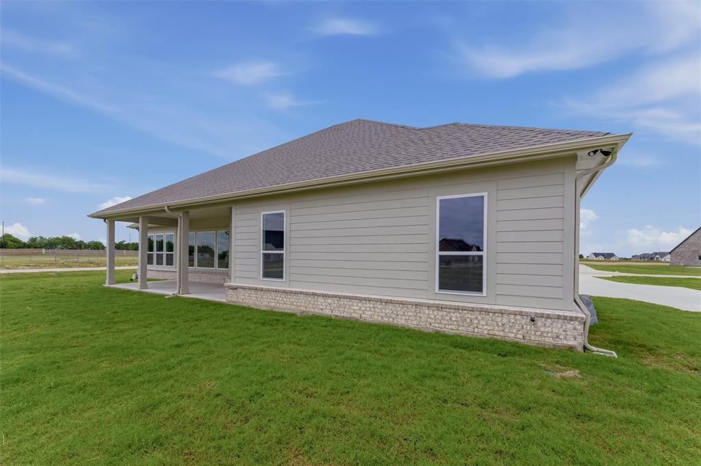 2204 Continent Court Krum, TX 76249 - Photo 28 of 28 Rear exterior showcasing an expansive covered patio, a stone and brick foundation, light-colored horizontal siding, and a shingle roof