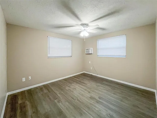 an empty room with wooden floor chandelier fan and windows
