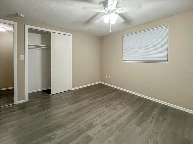a view of an empty room with wooden floor and a ceiling fan