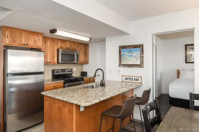 a kitchen with granite countertop stainless steel appliances a refrigerator a stove a sink a dining table and chairs with wooden floor