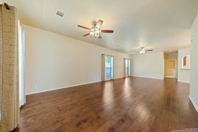 a view of an empty room with wooden floor and a ceiling fan