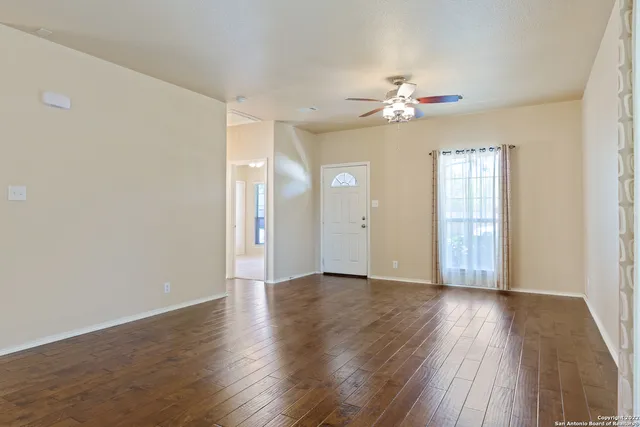 an empty room with wooden floor fan and windows