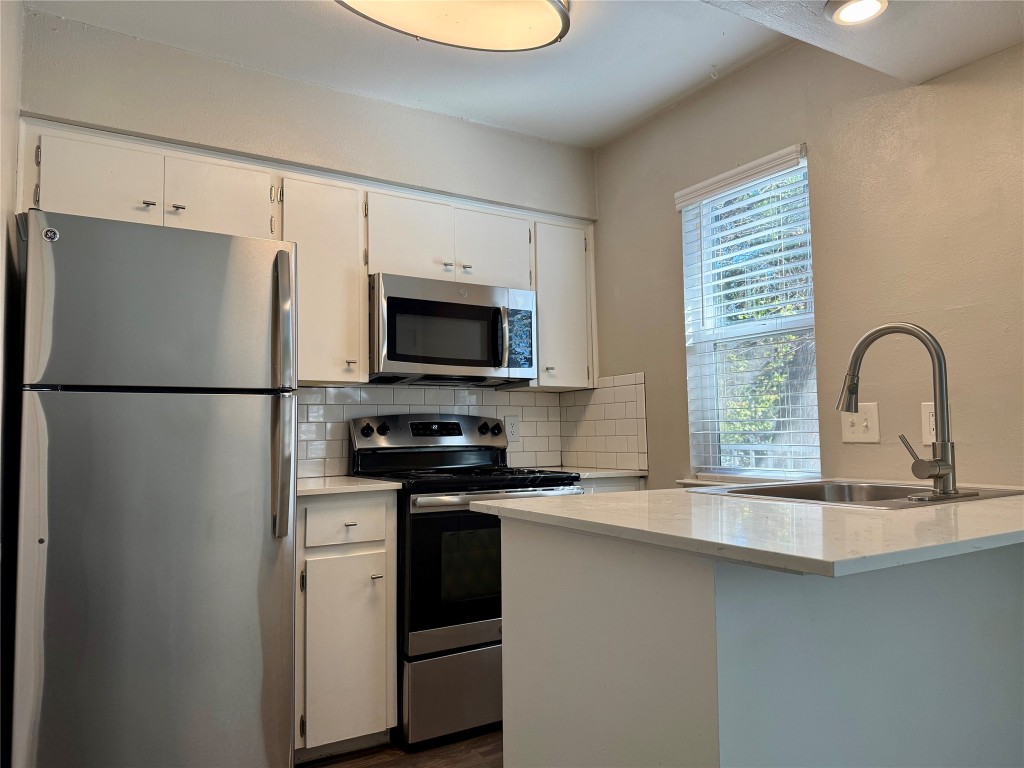 a kitchen with stainless steel appliances granite countertop a sink a stove a refrigerator a window and a sink