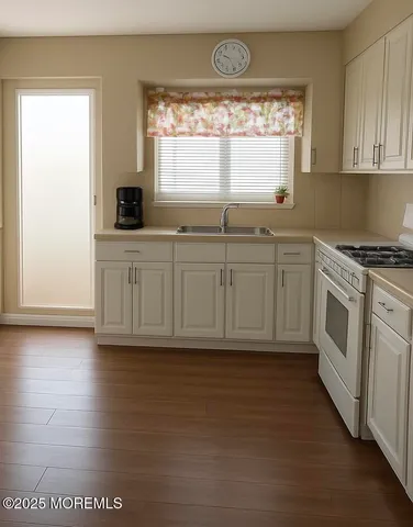 a kitchen with stainless steel appliances granite countertop a stove a sink and white cabinets with wooden floor