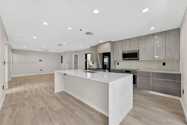 a large kitchen with stainless steel appliances a large counter top a stove a refrigerator and white cabinets