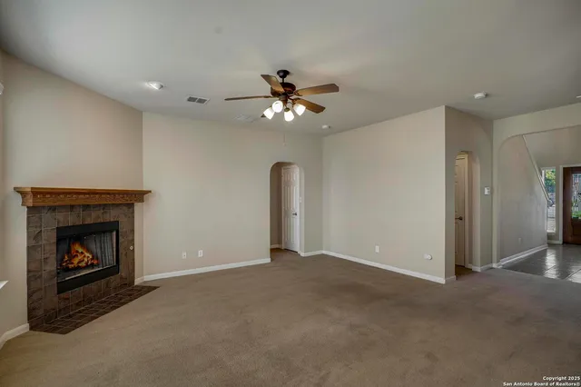 a view of an empty room with chandelier fan and fire place