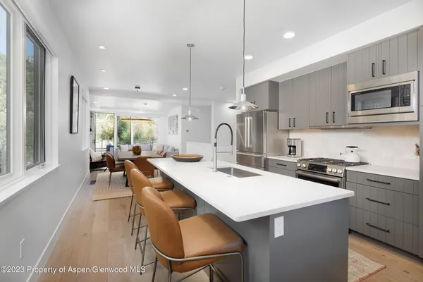 a kitchen with stainless steel appliances a stove a sink a kitchen island with chairs and wooden cabinets