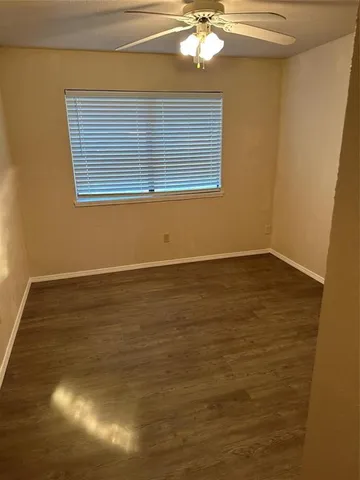 a view of an empty room with wooden floor and fan