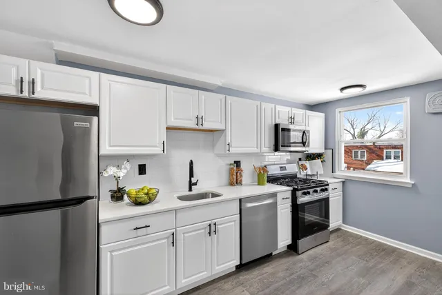 a kitchen with stainless steel appliances granite countertop a refrigerator a stove a sink dishwasher and white cabinets with wooden floor